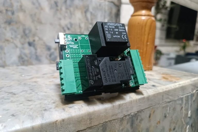 arka planda merdiven basamağı, ahşap korkuluk olan ve önplanda üzerinde elektronik kompenentler olan TNS otel rölesi görseli