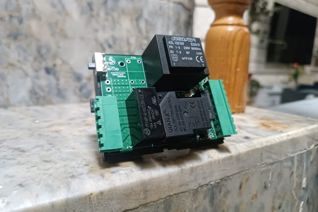 arka planda merdiven basamağı, ahşap korkuluk olan ve önplanda üzerinde elektronik kompenentler olan TNS otel rölesi görseli